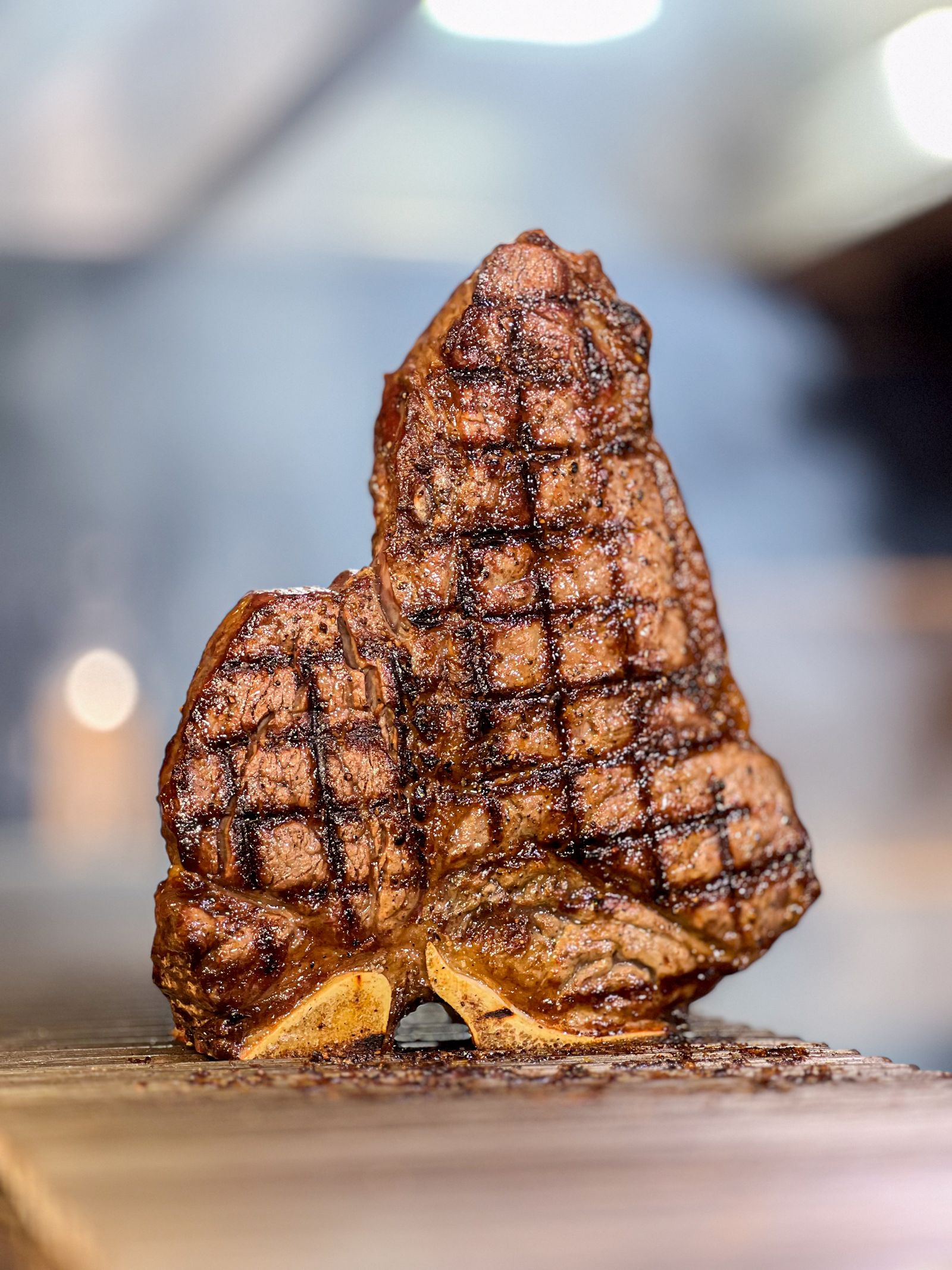 Bistecca alla fiorentina alta, con la crosta segnata dalla brace, in piedi sul tagliere di legno