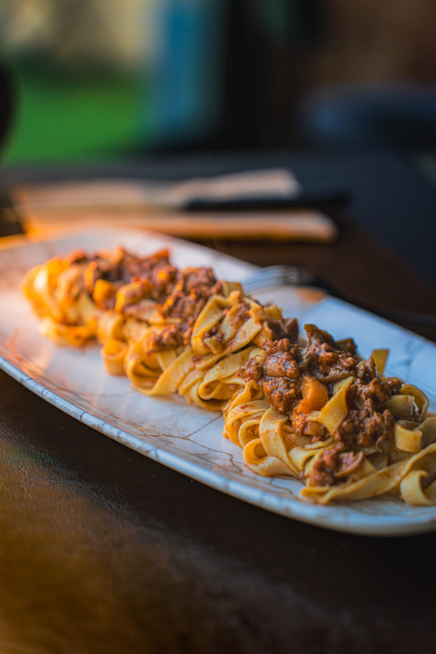 Pappardelle fresche all'uovo con ragù scuro, su piatto ovale in ceramica
