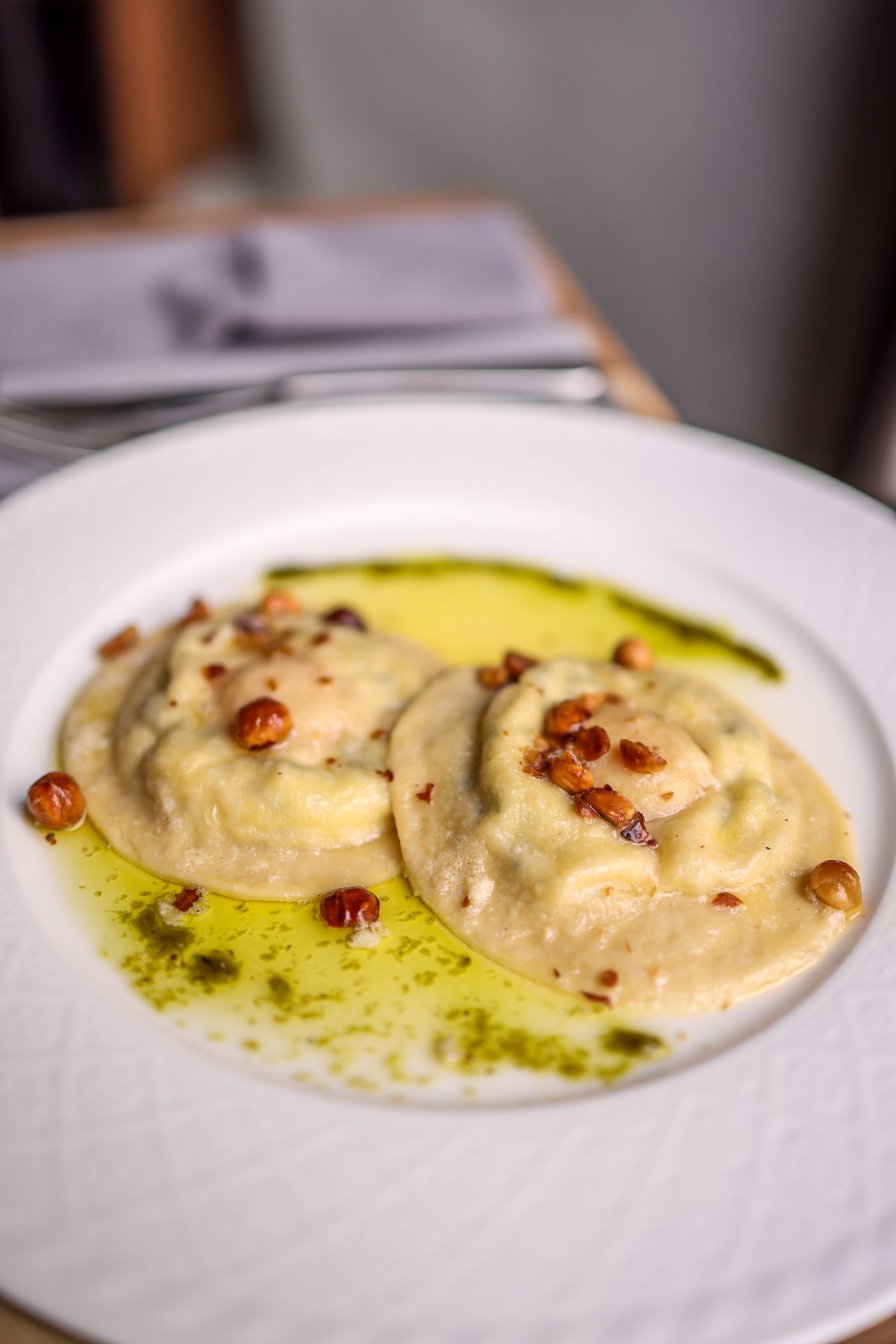Due grandi ravioli tondi su piatto chiaro, con olio alle erbe e noci tostate